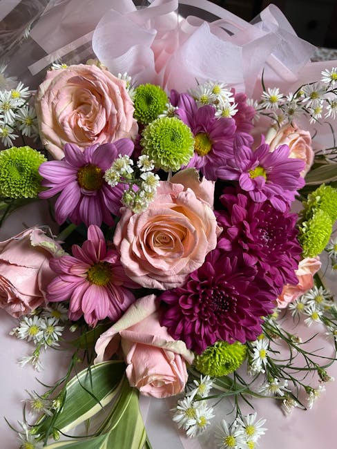 A vibrant floral bouquet featuring soft pink roses with delicate, layered petals, complemented by bright purple daisies with yellow centers, and vivid green chrysanthemums with round, textured blooms.