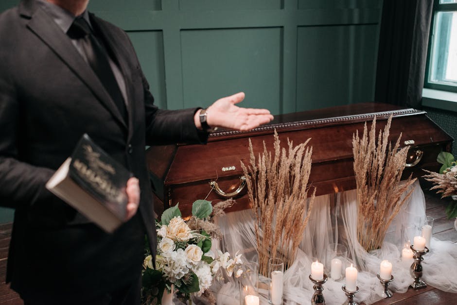 A floral arrangement positioned on a polished wooden surface, featuring tall, beige pampas grass stalks arranged vertically in the center, flanked by bouquets of white roses, pale cream lilies, and gr